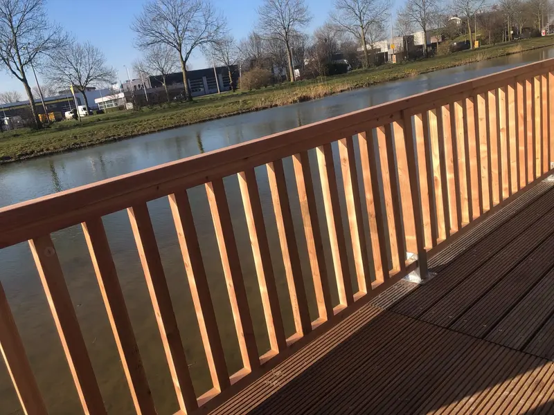 Houten balustrade met verticale spijlen op een vlonder langs een watergang, in laag zonlicht